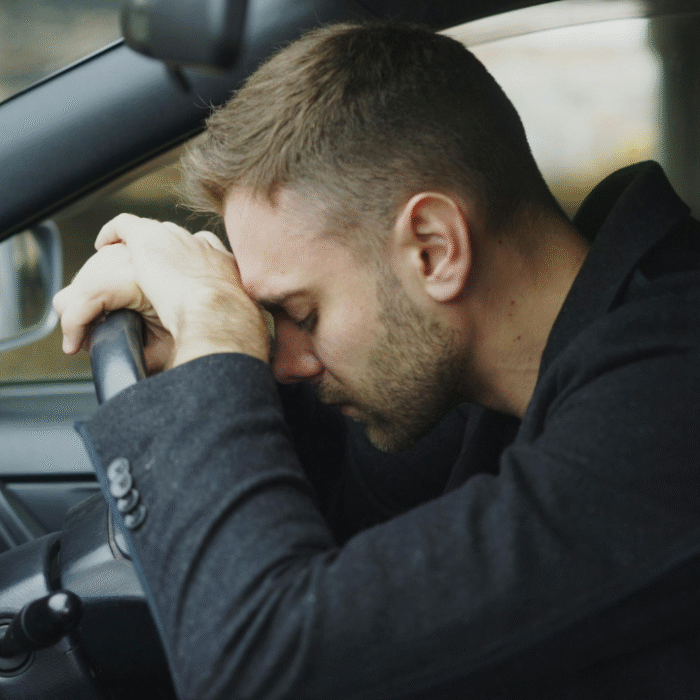 Tired man resting his head on the steering wheel of his car, illustrating fatigue and low energy in men